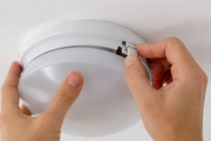 Mains qui déclipsent le cache d'un plafonnier blanc au plafond, mécanisme de fixation visible